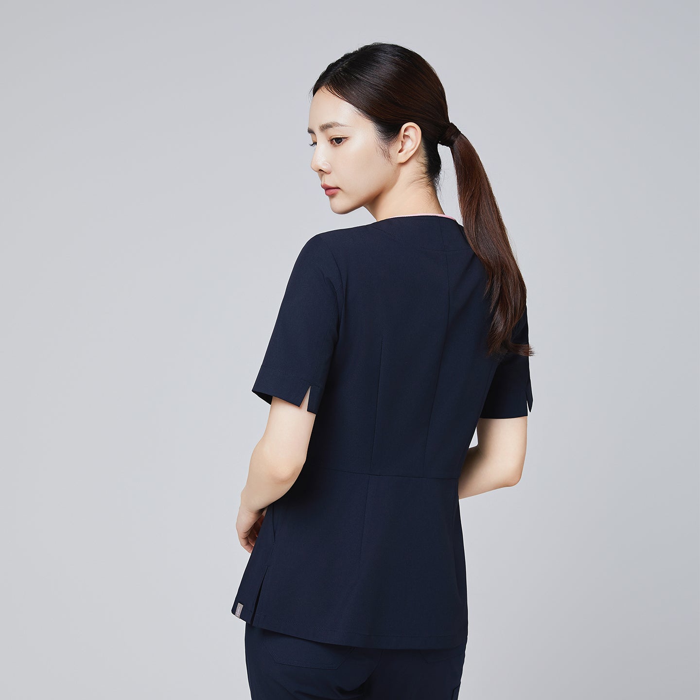 Image of Back view of a navy scrub top with short sleeves and tailored seams, modeled by a woman in a professional pose.Navy